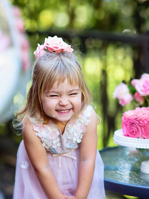 excited young girl in a party dress celebrating her birthday outside with a cake